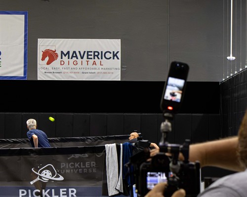 A courtside view of a pickleball match being captured on camera in front of a prominent Maverick Digital marketing banner.