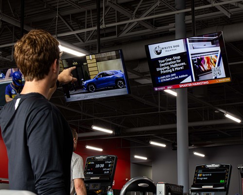 A gym member on a treadmill pointing directly at a local business advertisement running on a Maverick Digital screen.