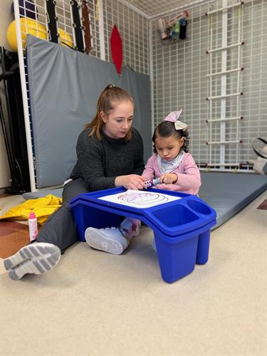 An occupational therapist works with Isabella to focus on fine motor skills development, such as using a marker to decorate a picture for her mom.
