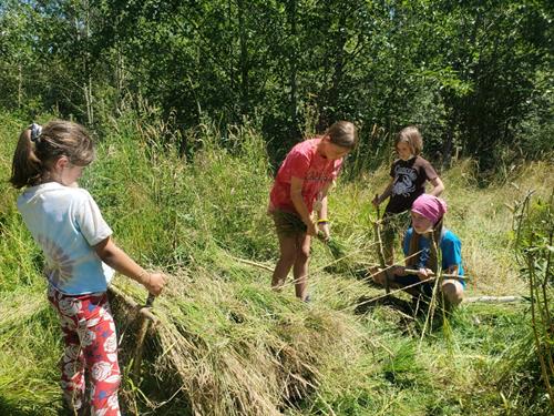 Kids using a 3 bear loom to weave a grass matt at summer camp