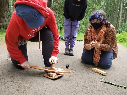 Adults practicing friction fire with a bow drill