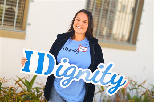 An IDignity student volunteer poses with the IDignity logo, showing her passion for serving. 