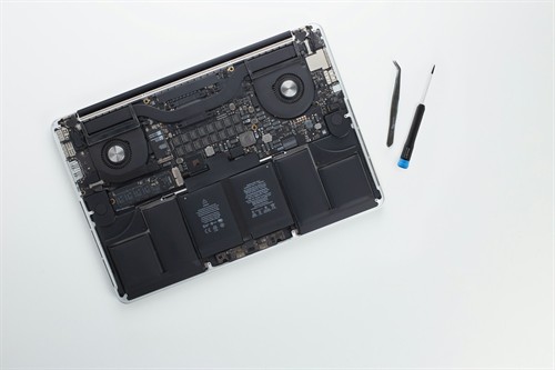 A MacBook upside down with its bottom cover removed and some tools nearby