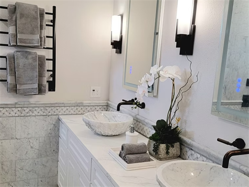 Carved marble vessel sinks, matte black fixtures, and backlit mirrors create a spa-inspired double vanity retreat.