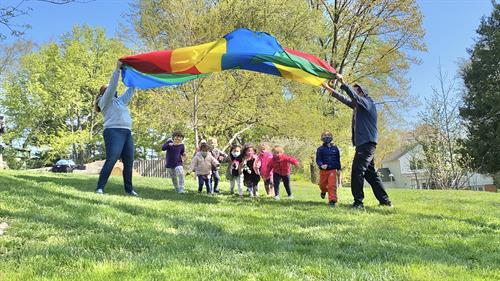Parachute play teaches colors, direction-following, and inspires gross motor fun.