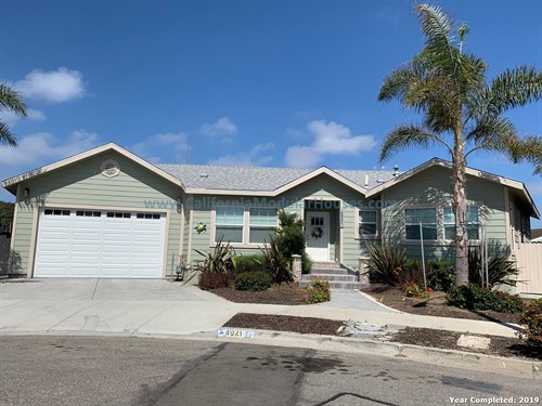 Single-story house with a light green exterior, white garage door, and front steps leading to a purple front door. California Modular Houses. Modular home construction California.  Prefab house.  Oxnard, Ventura County, CA.  