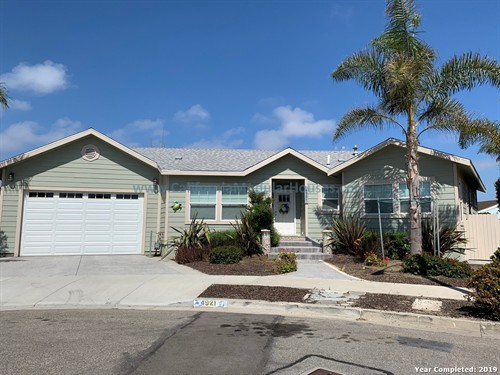 A light green, single-story house with a gray shingled roof, a two-car garage, a front porch with steps. California Modular Houses. Pre fab home.  Modular homes for California.  Casas prefabricadas.  Southern California.  