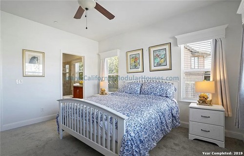 Bedroom with white walls.  There is a ceiling fan and windows with white curtains.  California Modular Houses. Pre fab home.  Modular homes for California.  Casas prefabricadas.  Southern California.  