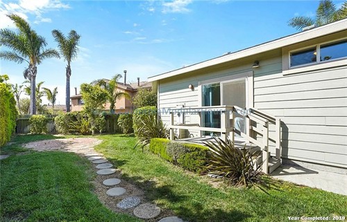 Backyard with a small wooden deck, sliding glass door, lush green grass, and various plants including palm trees.  California Modular Houses. Modular home construction California.  Prefab house.  Oxnard, Ventura County, CA.  
