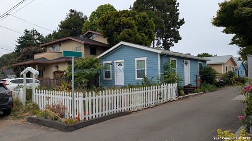 Colorful houses on a residential street with white picket fences, plants, and trees in California.