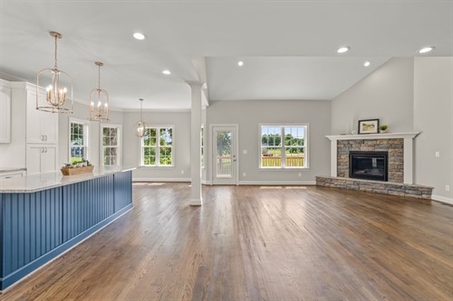 Bright open-concept space with vaiulted ceilings, hardwood floors, and a shite kitchen with bold blue island.