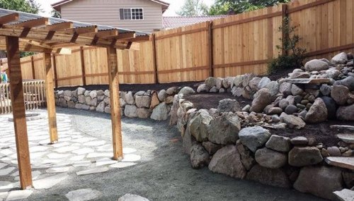 Rock retaining wall and pergola landscape design project in Oak Harbor, WA creating a structured and inviting backyard space.