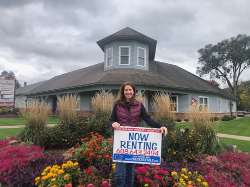 Woman holding a now renting sign in front of flower garden