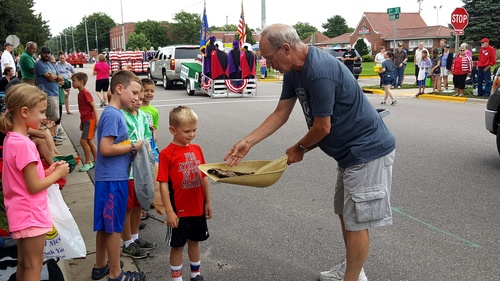 Man handing out cow chips in a shovel to kids at the Cow Chip parade