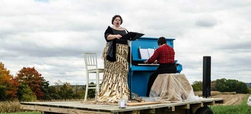 Man playing piano while woman is singing on a stage outside