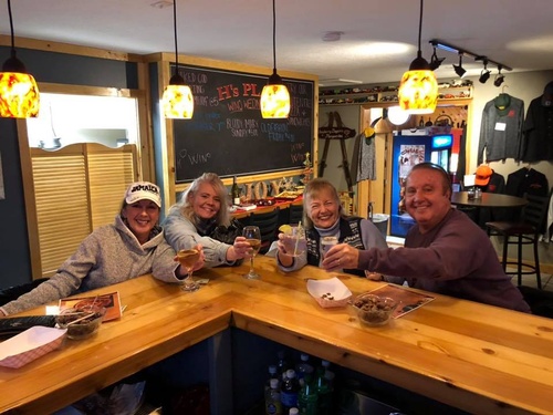 Group of four people cheering with drinks at bar at H's Place