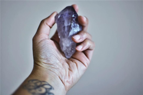 Image of a brown hand holding an amethyst crystal. 