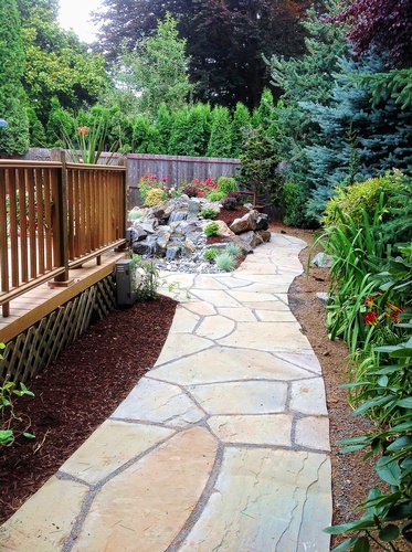 A Greenhaven Landscapes design customer's Vancouver WA backyard stone walkway path with wood deck and stone waterfall water feature