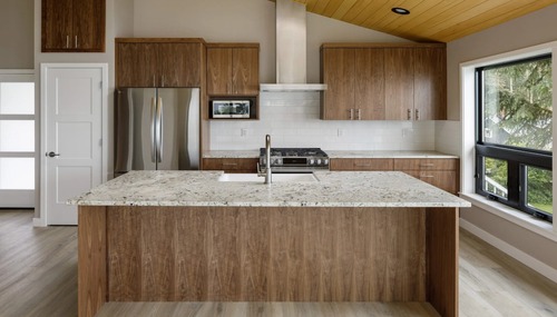 Modern custom kitchen with a large waterfall island, wood cabinetry, and quartz countertops by Dihedral Builders.